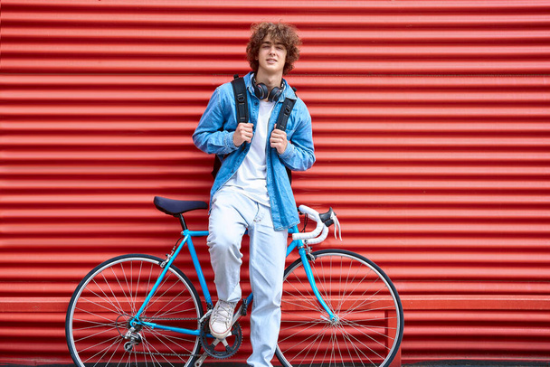 Mosolygó férfi támaszkodik a kerékpár és bordázott piros fal - Fotó, kép