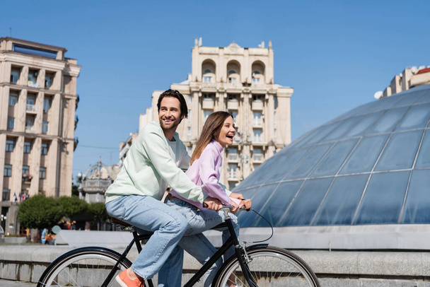 Веселая пара на велосипеде возле здания на городской улице  - Фото, изображение