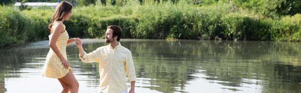 happy man holding hand of young woman in dress near lake, banner - Фото, зображення