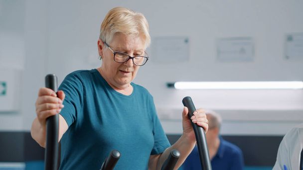 Oudere patiënt doet lichamelijke oefening op stationaire fiets - Foto, afbeelding
