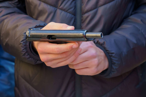Eine Waffe in den Händen eines jungen Mannes, selektiver Fokus. Nachladen von Waffen. Schießtraining. Regeln für das Halten und Tragen von Schusswaffen. Hintergrund mit Kopierraum - Foto, Bild