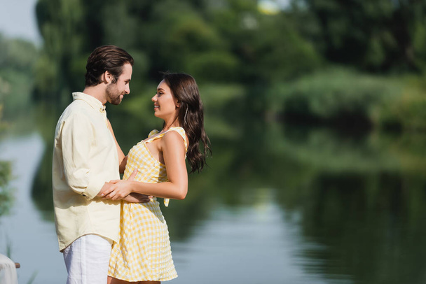 side view of pleased young couple looking at each other near lake - Foto, immagini
