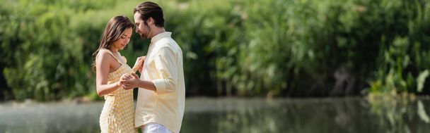 夏の服を着た幸せなカップルが湖の近くで手をつないで - 写真・画像