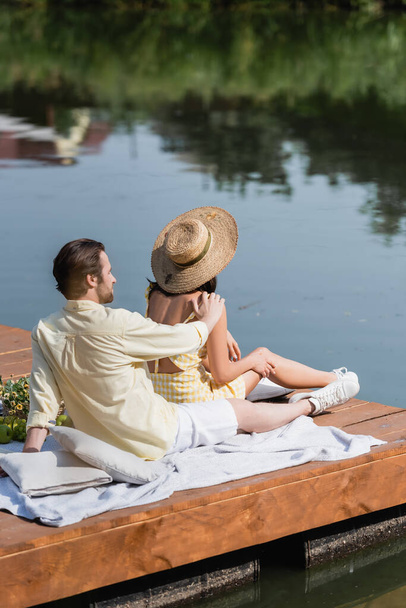 bearded man and woman in straw hat sitting on pier during picnic - Φωτογραφία, εικόνα