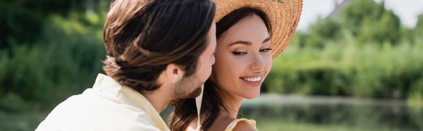 homme flou chuchotant à l'oreille d'une femme souriante en chapeau de paille, bannière - Photo, image