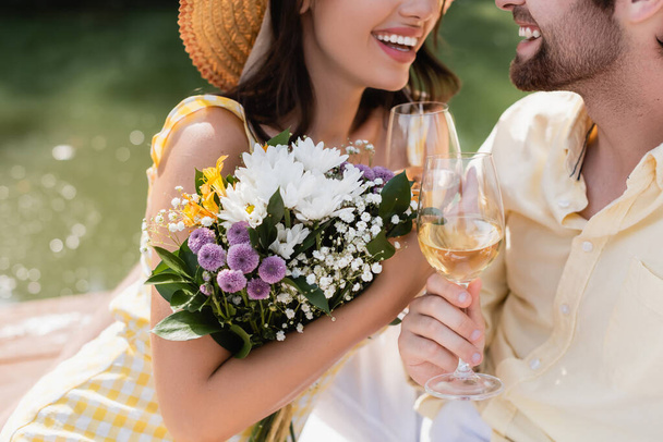 花の花束を持っている女性とボーイフレンドとクリンクグラスのクロップドビュー  - 写真・画像