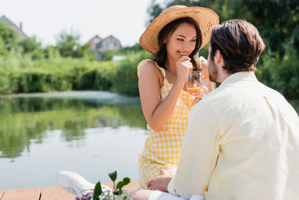 excited woman in straw hat holding glass of wine and looking at boyfriend  - Foto, Imagem