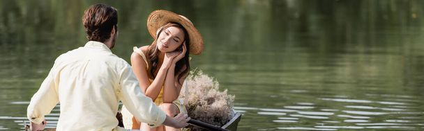 femme rêveuse en chapeau de paille regardant petit ami romantique pendant la promenade en bateau, bannière - Photo, image