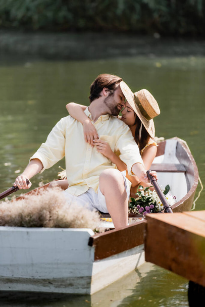 young woman in straw hat kissing man during romantic boat trip  - Φωτογραφία, εικόνα