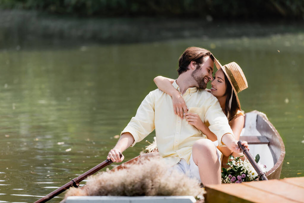 happy young woman in straw hat hugging man during romantic boat trip  - Foto, Imagen