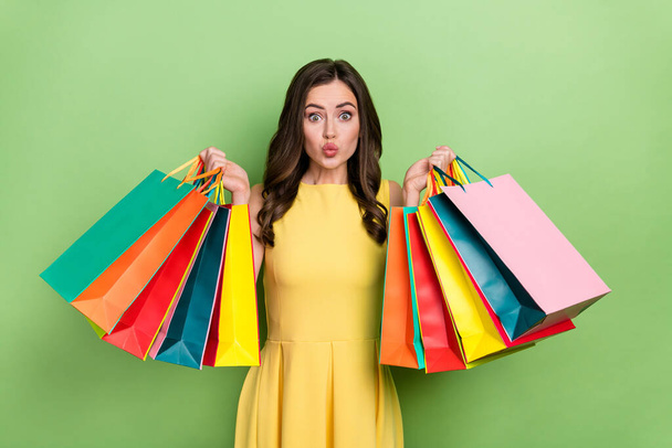 Portrait of attractive girly funky wavy-haired girl holding bags pout lips isolated over bright green color background - Foto, imagen