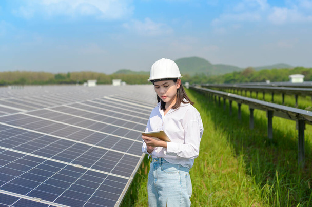 A female engineer wearing helmet in Photovoltaic Cell Farm or Solar Panels Field, eco friendly and clean energy. - Zdjęcie, obraz