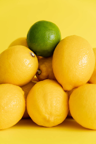 Close up view of green lime on lemons on yellow surface  - Φωτογραφία, εικόνα