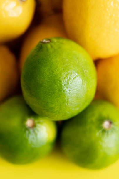Close up view of fresh green limes near blurred lemons on yellow surface  - Fotó, kép