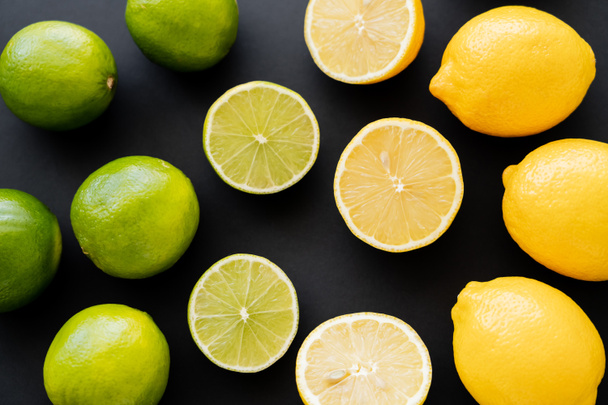 Flat lay of whole and cut lemons and limes on black background  - Fotó, kép