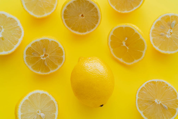 Top view of whole and halves of organic lemons on yellow surface  - Foto, afbeelding