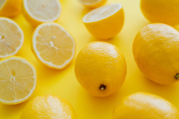 Close up view of fresh lemons near blurred halves on yellow surface  - Photo, Image