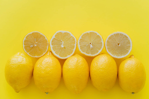 Top view of rows of whole and cut lemons on yellow surface  - Fotoğraf, Görsel