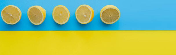 Bovenaanzicht van gesneden citroenen op blauwe en gele achtergrond, banner  - Foto, afbeelding