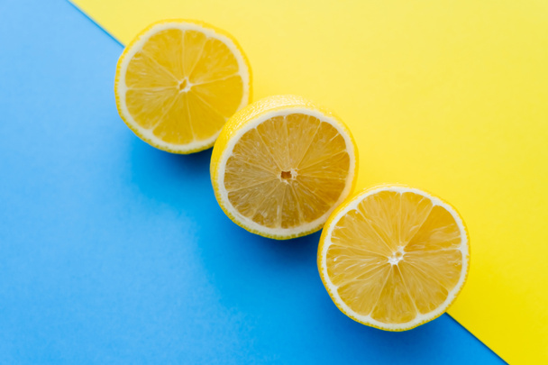 Vista dall'alto dei limoni tagliati su sfondo blu e giallo - Foto, immagini