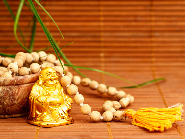 bol avec des perles de mala et statue de bouddha doré sur fond en bois avec des feuilles de plantes vertes. accessoire pour la méditation japa et la pleine conscience - Photo, image