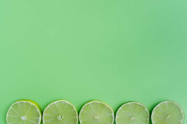 Top view of slices of limes on green background with copy space - Photo, image
