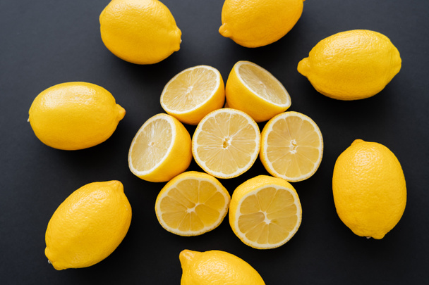Flat lay with cut and whole lemons on black background - Foto, Imagen