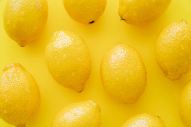 Top view of fresh lemons with droplets on peel on yellow surface - Fotografie, Obrázek