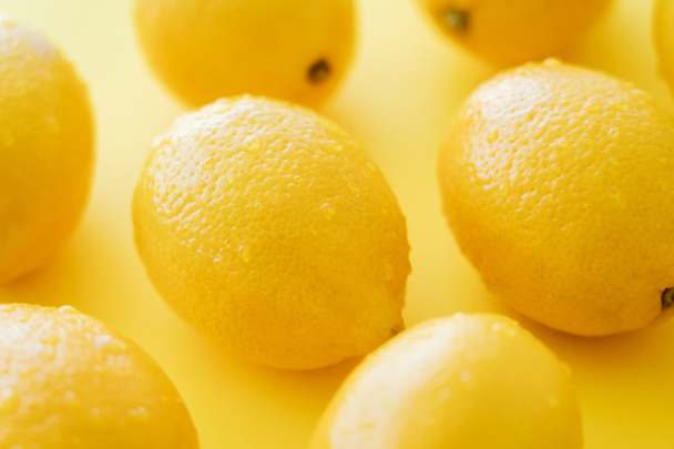 Close up view of organic and wet lemons on yellow surface - Fotó, kép