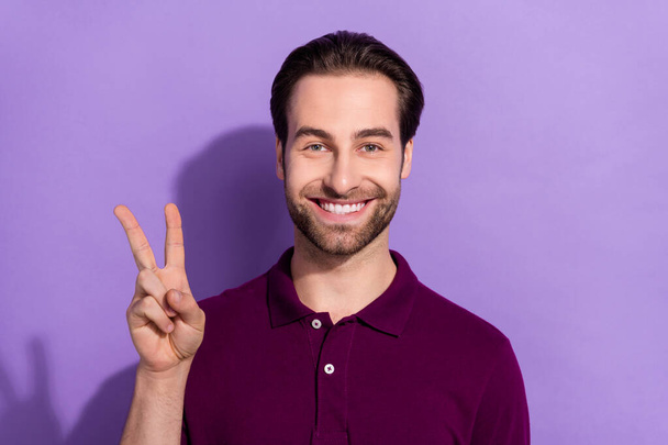 Photo of funky young brunet guy show v-sign wear purple t-shirt isolated on violet color background - Fotografie, Obrázek