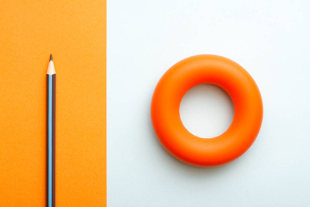 Orange rubber hand gripper and a pencil. Healthy lifestyle physical activity concept flat lay. - Zdjęcie, obraz