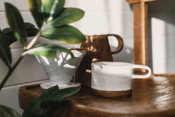 Альтернативний метод приготування кави. Сучасна керамічна чашка, чайник і дріпка для кави на сонячному світлі на дерев'яному стільці і листя тіні в стильній сонячній кімнаті
 - Фото, зображення