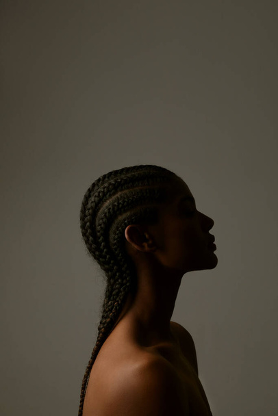Vertical side portrait of African young woman with braids posing on dark wall. - Фото, зображення