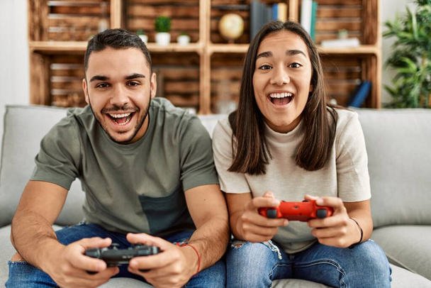 Joven pareja latina sonriendo feliz jugando videojuego en casa. - Foto, Imagen