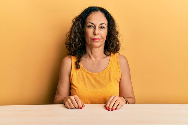 Beautiful middle age woman wearing casual clothes sitting on the table looking sleepy and tired, exhausted for fatigue and hangover, lazy eyes in the morning.  - Photo, Image