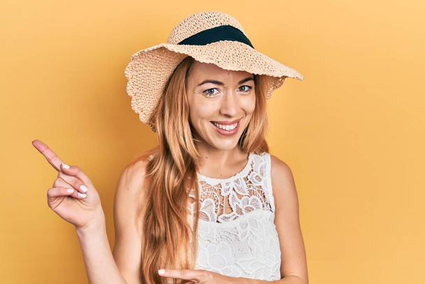 Young caucasian woman wearing summer hat smiling and looking at the camera pointing with two hands and fingers to the side.  - Foto, imagen