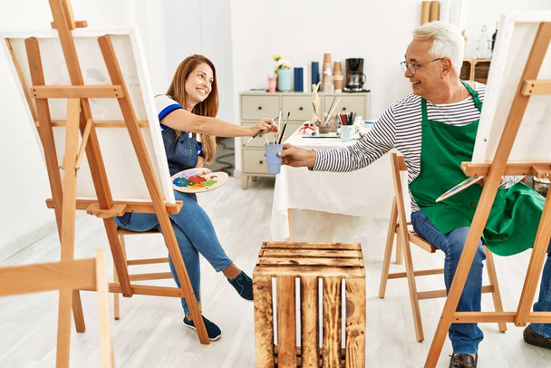 Dos artistas de mediana edad sonriendo feliz pintura en el estudio de arte. - Foto, imagen