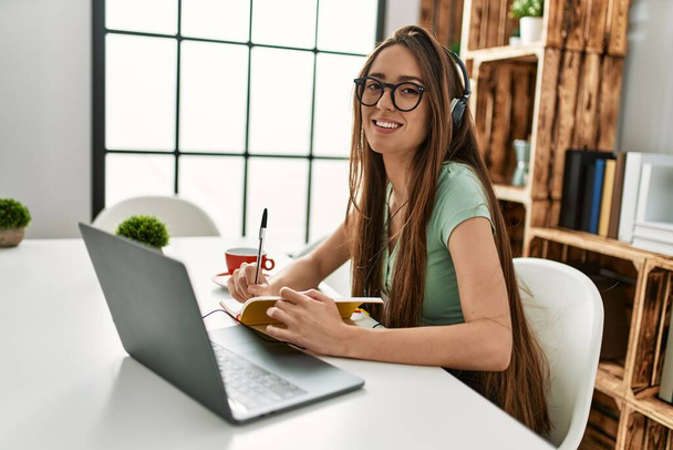 Fiatal spanyol nő használja laptop és írás a könyv ül az asztalon otthon - Fotó, kép