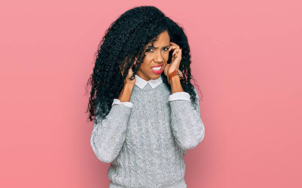 Mujer afroamericana de mediana edad que usa ropa casual que cubre las orejas con dedos con expresión molesta por el ruido de la música fuerte. concepto de sordo.  - Foto, Imagen