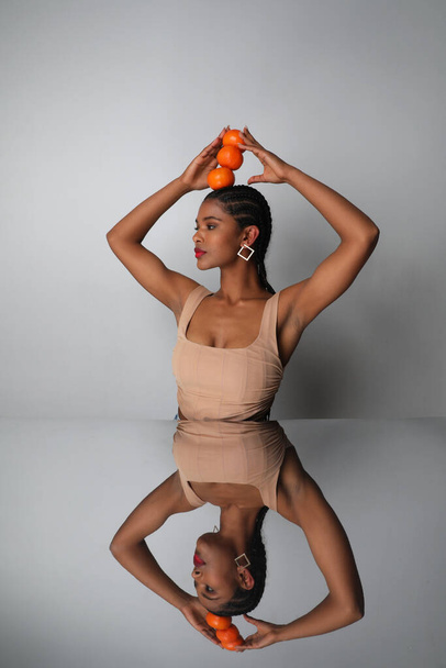 Beautiful African young woman poses with oranges on her head on white wall. - Foto, imagen