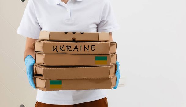 Ένας άνδρας κρατά ένα κουτί βοήθειας για τους Ουκρανούς πρόσφυγες και τους φτωχούς πολίτες που βρίσκονται σε έναν πόλεμο μεταξύ Ουκρανίας και Ρωσίας. Σχέδιο ανθρωπιστικής βοήθειας. Δωρεά για πρόσφυγες. - Φωτογραφία, εικόνα