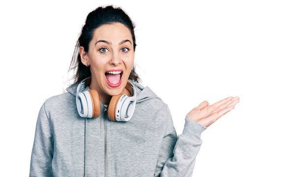 Mujer hispana joven usando ropa de gimnasio, usando auriculares y reloj inteligente celebrando loco y sorprendido por el éxito con los ojos abiertos gritando emocionado.  - Foto, Imagen