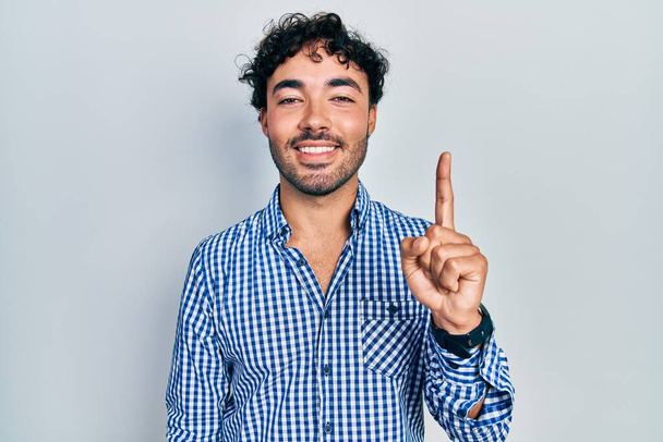 Jovem hispânico vestindo roupas casuais mostrando e apontando para cima com o dedo número um enquanto sorri confiante e feliz.  - Foto, Imagem