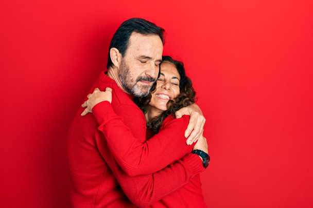 Μεσήλικες ζευγάρι ισπανόφωνων γυναικών και αντρών που αγκαλιάζονται και στέκονται μαζί αγκαλιάζοντας τον εαυτό τους χαρούμενο και θετικό, χαμογελώντας σίγουροι. αυτοαγάπη και αυτοφροντίδα  - Φωτογραφία, εικόνα