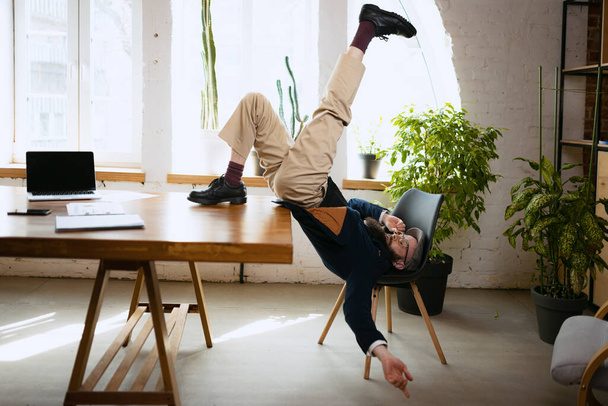 Jonge man met baard, kantoorbediende die plezier heeft, yoga doet op houten tafel in modern kantoor op het werk met gadgets. Begrip bedrijf, gezonde levensstijl, sport, hobby - Foto, afbeelding