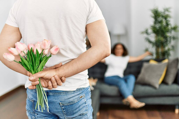 Mężczyzna zaskakujący swoją żonę kwiatami w domu. - Zdjęcie, obraz