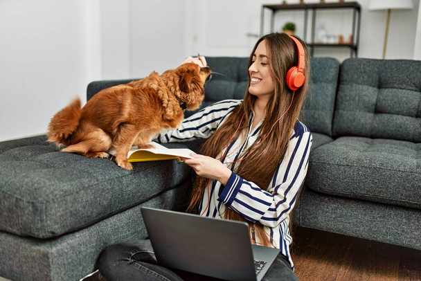 Young hispanic woman using laptop studying sitting on floor with dog at home - Foto, Bild