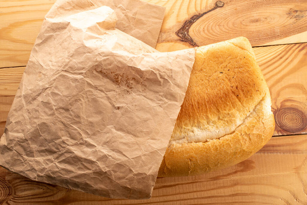 Bir somun aromalı buğday ekmeği bir torba kağıt içinde, ahşap bir masanın üzerinde, yakın plan, üst manzara. - Fotoğraf, Görsel