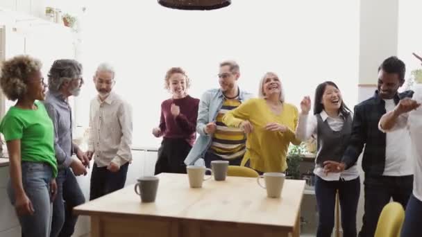 Gelukkige multiraciale mensen met verschillende leeftijden en etniciteiten die plezier hebben met dansen terwijl ze thuis een kopje koffie drinken - Video