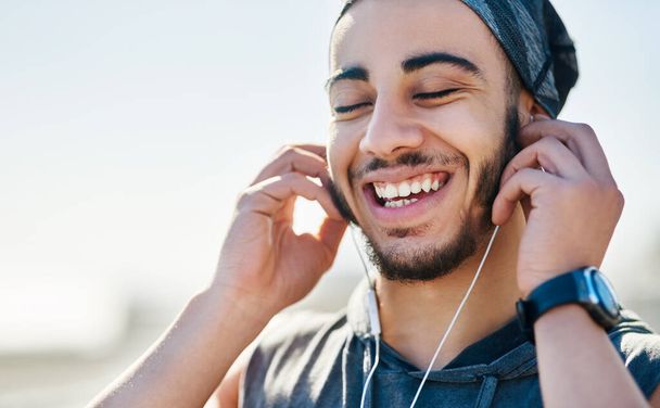 The groove is getting him into the fitness zone. Shot of a sporty young man listening to music while exercising outdoors. - 写真・画像